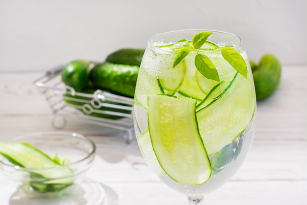 Água refrescante com fatias de pepino e manjericão folhas em um copo e pepinos em uma cesta