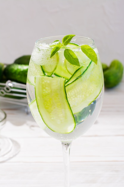 Água refrescante com fatias de pepino e manjericão folhas em um copo e pepinos em uma cesta