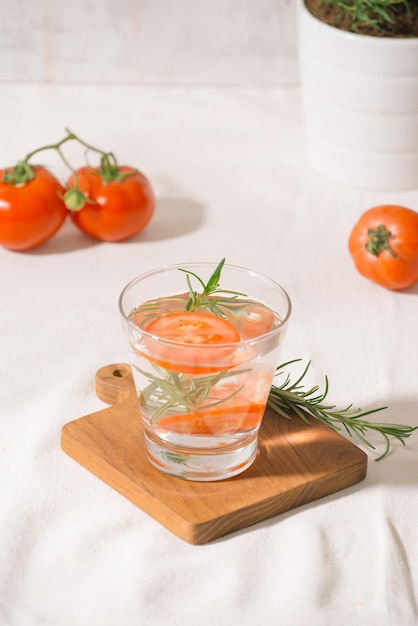 Água refrescante deliciosa com alecrim e tomate em copo na mesa