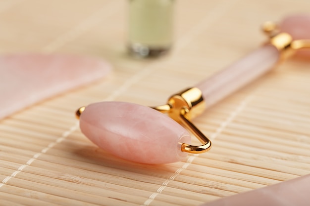 Gua sha Massage aus natürlichem Rosenquarz-Roller, Jadestein und Öl auf Bambushintergrund für Gesichts- und Körperpflege.