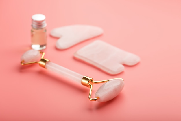 Gua sha Massagewerkzeug aus natürlichem rosa Quarzroller, Jadestein und Öl auf rosa Hintergrund für Gesichts- und Körperpflege. Teil der traditionellen chinesischen Medizin