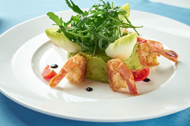 Guacamole de aguacate con camarones, rúcula y tomates cherry en un plato blanco sobre un mantel azul. De cerca. comida mexicana