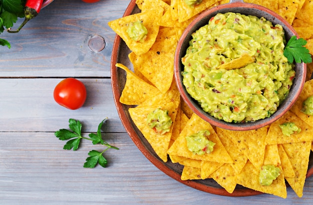 Guacamole Avocado, Limette, Tomate, Zwiebel und Koriander, serviert mit Nachos - traditioneller mexikanischer Snack. Flach liegen. .