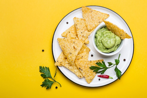 Guacamole latino-americano tradicional com nachos de chips de milho em fundo amarelo.