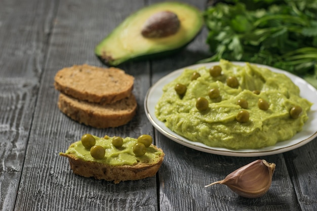 Guacamole mit grünen Erbsen und Brot auf einem rustikalen Tisch. Diät-vegetarisches mexikanisches Essen Avocado. Rohkost.