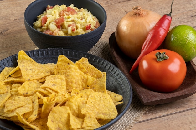 Guacamole mit Tortillas mit Zutaten im Hintergrund.