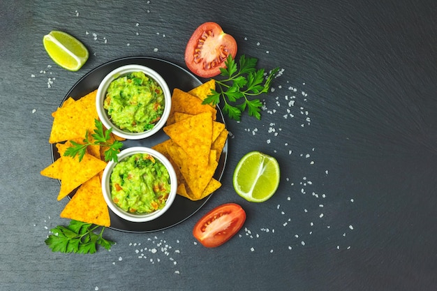 Foto guacamole y nachos con ingredientes en el fondo de un tablero de piedra negra espacio de copia de vista superior