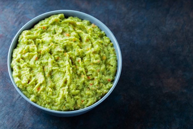 Guacamole en un recipiente gris sobre un fondo oscuro. Tazón de fuente de salsa de guacamole de aguacate con ingredientes frescos. Copie el espacio. Vista superior