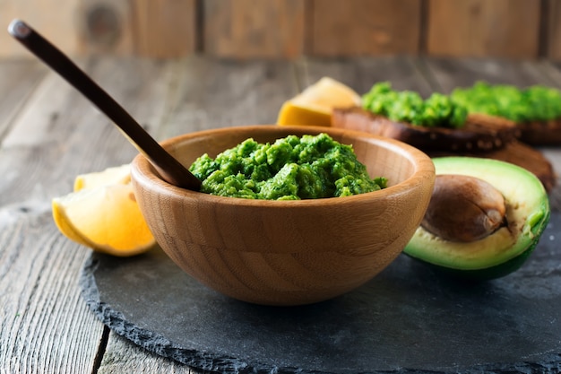 Guacamole de salsa mexicana tradicional en tazón de bambú, limón y medio aguacate cortado en superficie de madera vieja. Enfoque selectivo. Lugar de texto.