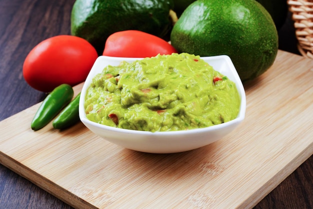 Guacamole servido em um prato branco sobre uma mesa de madeira. Ingredientes do Guacamole.