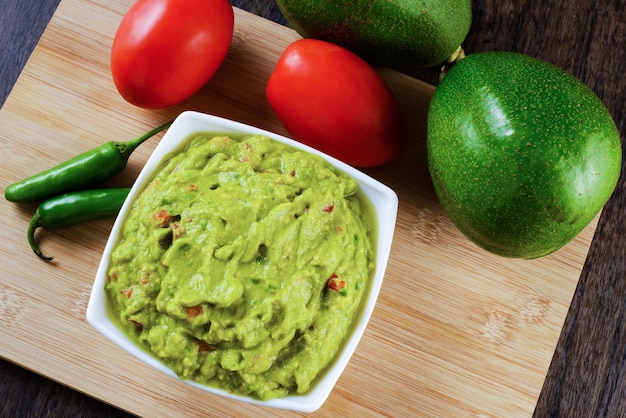 Guacamole servido em um prato branco sobre uma mesa de madeira. Ingredientes do Guacamole.