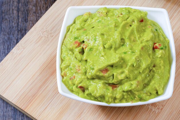 Guacamole servido en plato blanco sobre mesa de madera. Recipiente aislado con guacamole.