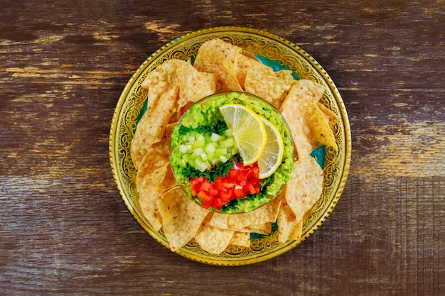 Guacamole verde con nachos y aguacate sobre fondo de madera