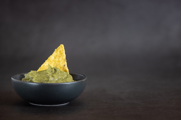 Guacamole verde con nachos en un tazón sobre fondo oscuro