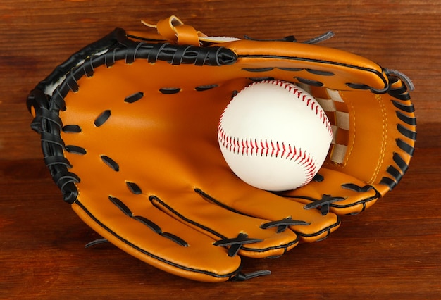 Guante de béisbol y pelota sobre fondo de madera