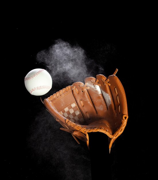 Guante de cuero guante de recibir golpe de pelota de béisbol y polvo tierra explotar en el aire bola de béisbal lanzar y golpear al centro del guante de guante fondo negro aislado acción de congelación