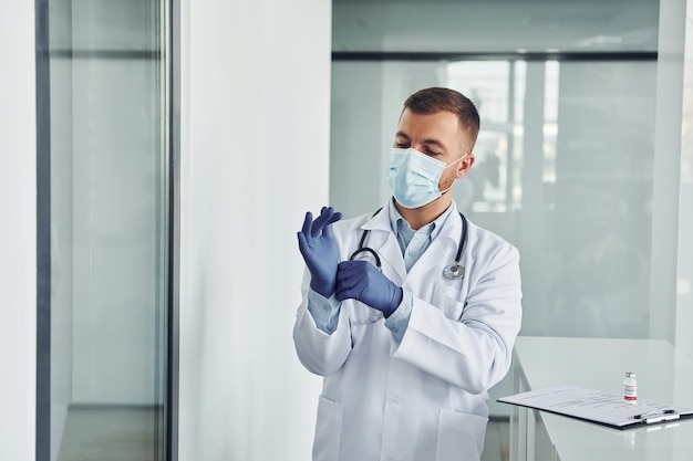 Foto en guantes azules, el médico profesional con bata blanca está en la clínica.