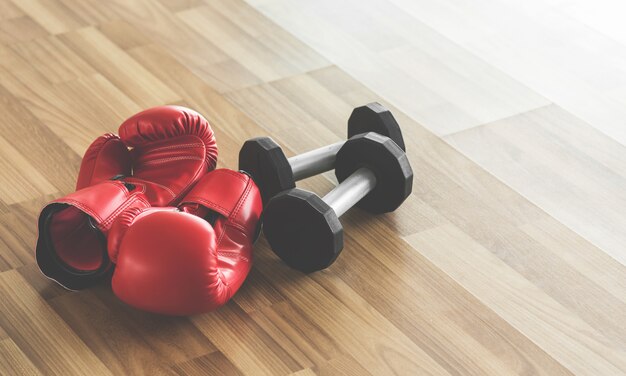 Guantes de boxeo rojos con pesas en el piso de madera.