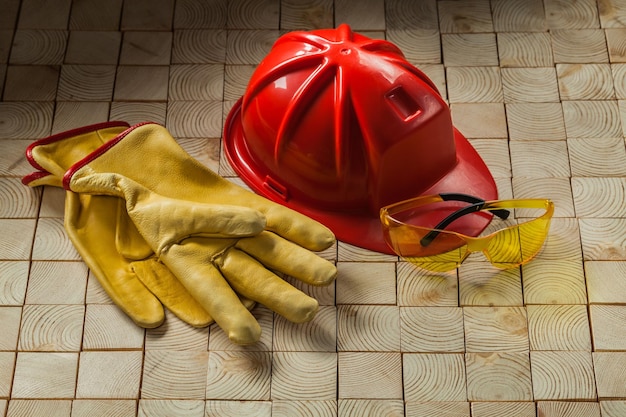 Guantes de construcción gafas y casco rojo sobre fondo de madera