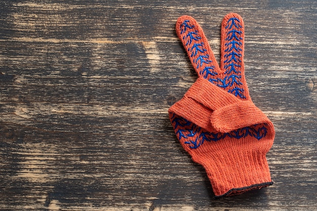 Los guantes de construcción naranja muestran el signo de la victoria en madera