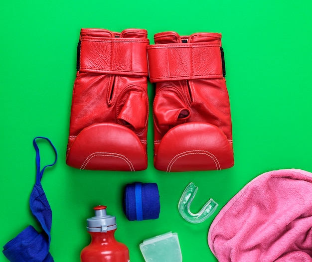 Guantes de cuero rojos, una botella de agua de plástico, una toalla rosa y una venda textil azul.