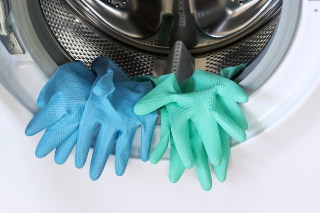 Guantes de goma azules y verdes en una lavadora abierta.