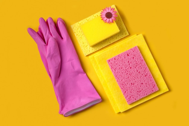 Guantes de goma y esponjas para lavar sobre un fondo amarillo.