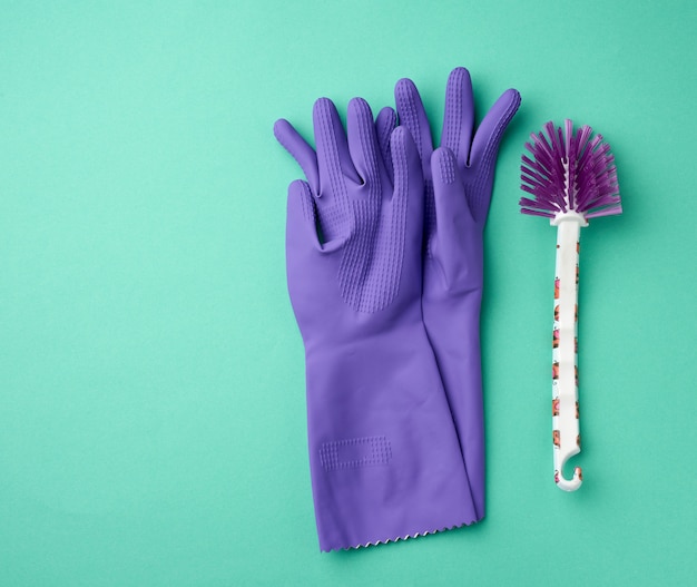 Guantes de goma morados para limpiar y un cepillo blanco sobre una superficie verde