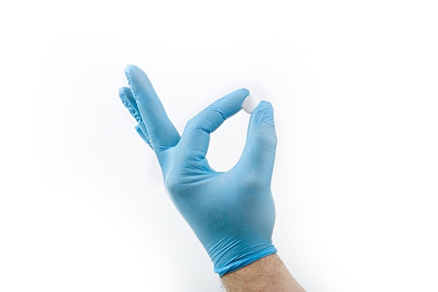 Guantes de goma o látex médicos azules con tableta, medicina, vitamina en la mano masculina aislada en un blanco