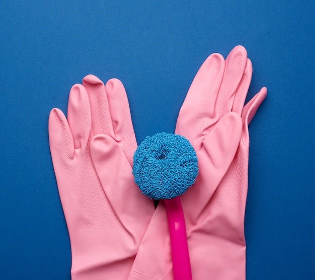 Guantes de goma rosa para limpiar, cepillos sobre un fondo azul.
