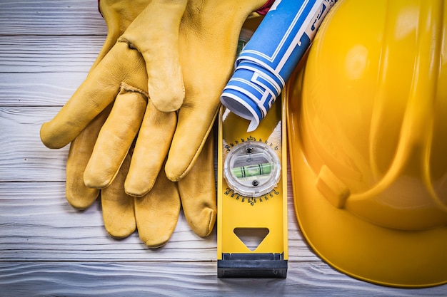 Guantes protectores que construyen el nivel de construcción de planos azules del casco en el tablero de madera.