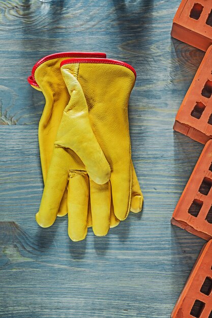 Guantes de seguridad de cuero ladrillos rojos en concepto de construcción de tablero de madera.