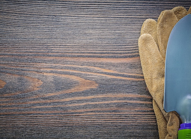 Guantes de seguridad de cuero con pala de metal en concepto de jardinería de espacio de copia de tablero de madera