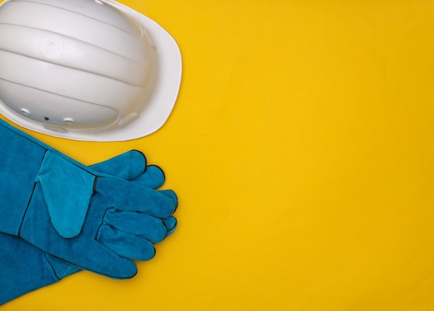 Guantes de trabajo y casco de seguridad de construcción sobre fondo amarillo. Vista superior. Copia espacio