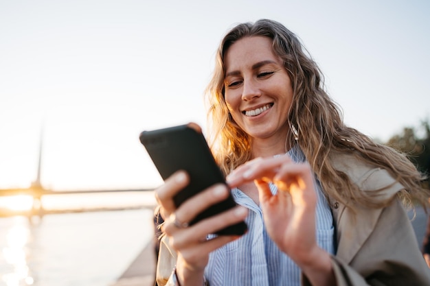 Foto guapa joven sonriente con teléfono móvil caminando por la calle