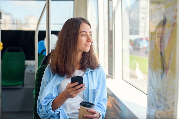 La guapa pasajera se sienta con el teléfono inteligente mientras se mueve en el moderno tranvía o metro. Viaje en transporte público.