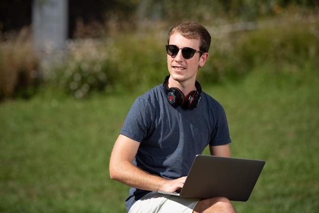 Guapo adolescente rubio sonriente trabajando en su computadora al aire libre