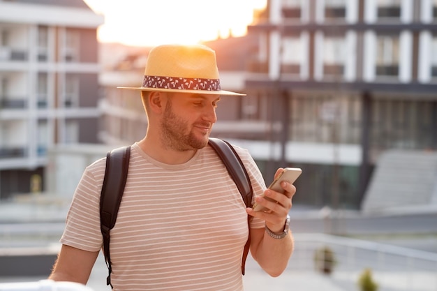 Guapo adulto hombre barbudo rubio de mediana edad con sombrero para el sol con teléfono móvil mensajes de texto chateando al aire libre Sonriente feliz turista caucásico usando teléfono inteligente navegando por internet