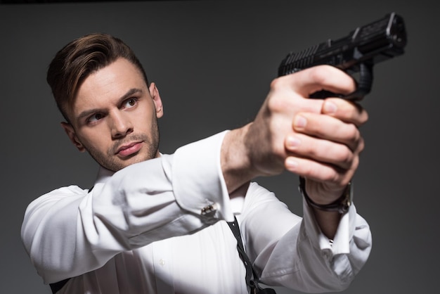 Guapo agente secreto apuntando con pistola aislado en gris