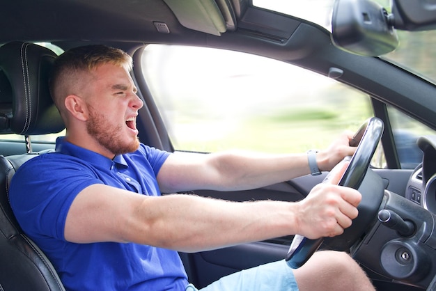 Guapo, asustado, temeroso, conductor, joven, hombre asustado, sorprendido por tener un accidente conduciendo un automóvil rápido en la carretera, sosteniendo el volante del automóvil Desabrochado por un cinturón de seguridad Violación de tráfico