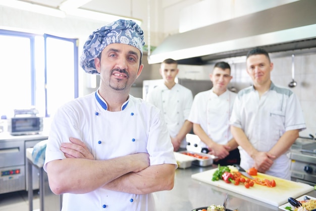 Guapo chef vestido con uniforme blanco decorando ensalada de pasta y pescado de marisco en la cocina moderna