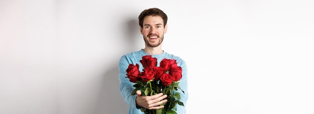 Guapo chico barbudo estira las manos dando ramo de rosas y sonriendo trae flores en romántico