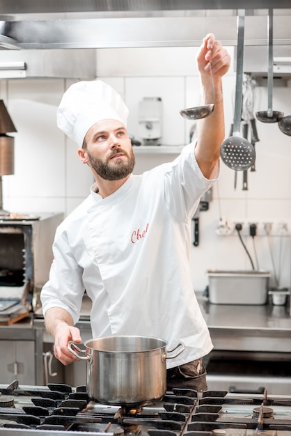 Guapo cocinero cocinar comida con sartén y cuchara en la cocina del restaurante