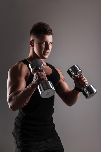 Guapo culturista hombre atleta modelo con peinado en ropa deportiva negra de moda entrenamiento con pesas de metal en la oscuridad