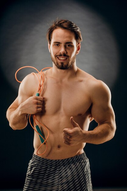 Un guapo culturista masculino con una cuerda en las manos sobre un fondo oscuro