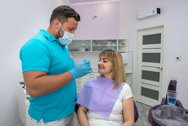 Guapo dentista masculino en una máscara examina los dientes de un paciente