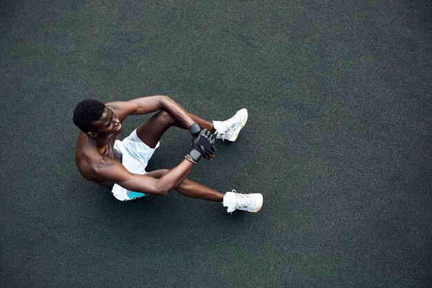 Guapo deportista afroamericano sentado en la calle mientras toma un descanso después de entrenar Hombre negro descansando después del entrenamiento