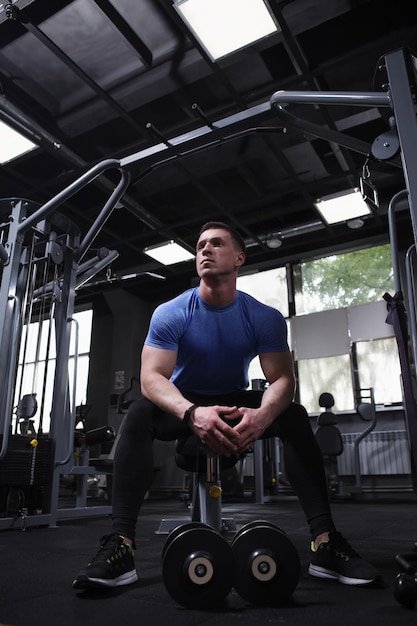 Foto guapo deportista musculoso descansando después de hacer ejercicio con pesas