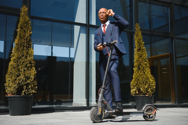 Guapo empresario africano montando scooter eléctrico al aire libre