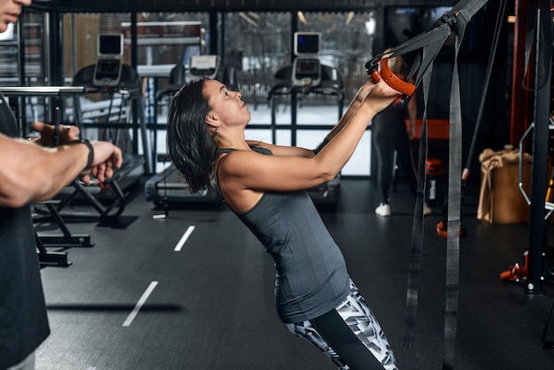 Foto guapo entrenador masculino con cuerpo atlético ayuda a la chica cliente a realizar ejercicios adecuados en el simulador el concepto de entrenamiento con un entrenador